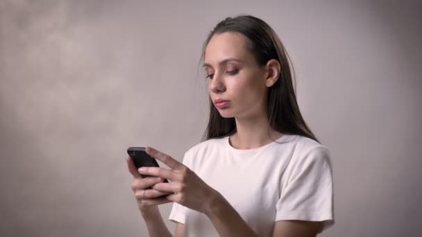 Ernstige sexy brunette meisje is het typen van bericht op de smartphone, communicatieconcept, grijze achtergrond — Stockvideo