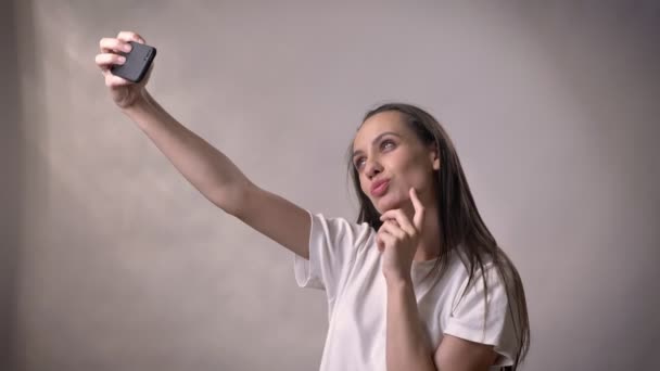 Giovane ragazza bruna sexy sta facendo selfie su smartphone, concetto di comunicazione, sfondo grigio — Video Stock