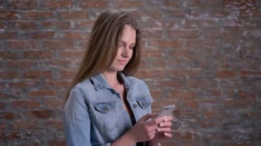 Genç Sevimli Kadın tipik smartphone, tuğla backgorund, iletişim kavramı üzerinde haber