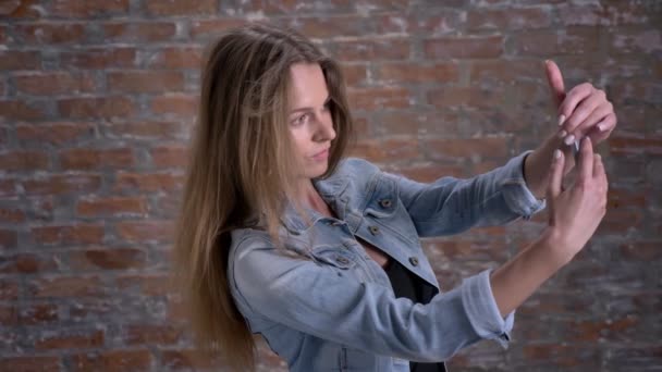 Jeune femme mignonne fait selfie sur smartphone, brique backgorund, concept de communication — Video