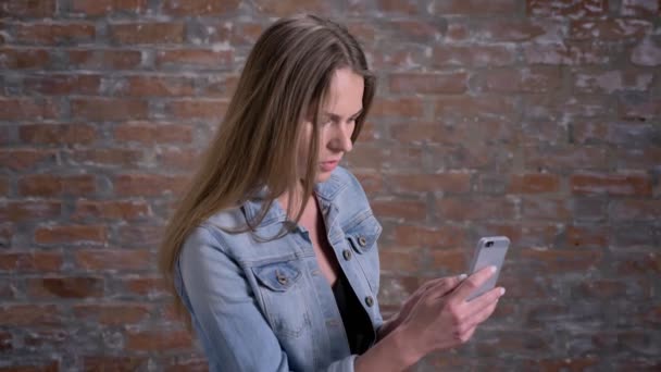 Jeune femme mignonne parle dans le chat vidéo sur smartphone, brique backgorund, concept de communication — Video