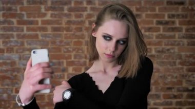 Dumanlı gözler kızla büyüleyici genç seifie onun smartphone, iletişim kavramı, tuğla arka plan yapmak
