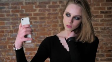 Dumanlı gözler ile genç çekici kız seifie yapmak üstünde onun smartphone, göz kırpıyor, iletişim kavramı, tuğla arka plan