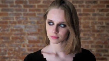 Dumanlı gözler ile genç çekici kız başını sallayarak, oynuyor saç, düşünme kavramı, tuğla arka plan