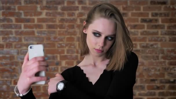 Молода чарівна дівчина з димчастими очима робить сейф на своєму смартфоні, концепція спілкування, цегляний фон — стокове відео