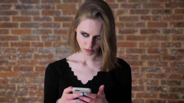 Fiatal szexi lány, füstös szemek gépelés üzenet a smartphone, gondolkodás fogalma, a kommunikáció fogalma tégla háttér — Stock videók