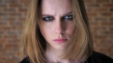 Genç seksi dumanlı gözler ile tiksinti kız kameraya, izliyor tuğla arka plan aşağı, yatıştırıcı arka plan bulanık