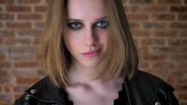 Dumanlı gözler ile genç üzgün kız kameraya, izlerken gülümseyerek, dudak, düşünme kavramı, tuğla arka plan ısırma