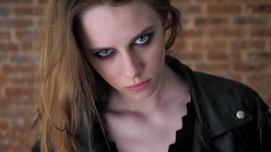 Dumanlı gözler ile genç seksi tiksinti kız kamera, saç yüz, yakın gözler, tuğla arka plan, arka plan bulanık izliyor