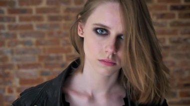 Dumanlı gözler ile genç seksi kendine güvenen kız kameraya, tuğla arka plan izliyor