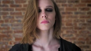 Dumanlı gözler ile genç seksi ciddi kız kameraya, izliyor kapatın onu gözler, tuğla arka plan