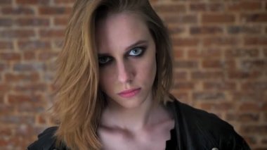 Dumanlı gözler ile genç seksi güçlü kız kameraya, tuğla arka plan bakıyor