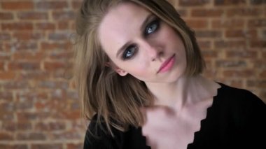 Dumanlı gözler ile genç çekici kız kameraya, izlerken gülümsüyor, kavram, tuğla arka plan flört