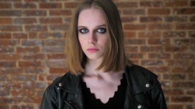 Dumanlı gözler ile genç seksi ciddi kız kameraya, tuğla arka plan izliyor