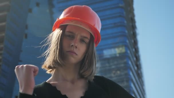 Joven chica fuerte constructor con aldea está mostrando puño en el día en verano, concepto de edificio, concepto urbano, edificio sobre fondo — Vídeo de stock