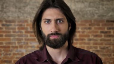 Sakallı genç ciddi esmer adam kameraya, tuğla arka plan izliyor