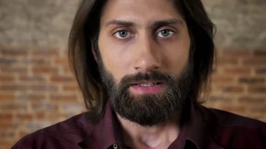 Genç sakallı esmer adam kameraya, tuğla arka plan izliyor korkmuş