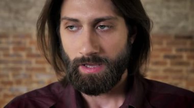 Sakallı genç esmer adam durum, tuğla arka plan kabul eder..