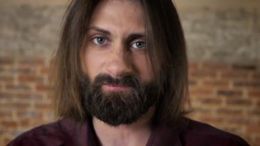 Sakallı genç öfkeli esmer adam izliyor kamera, yumruk, tuğla arka plan