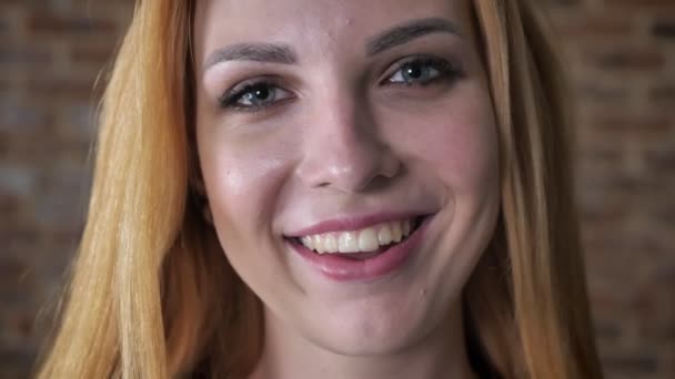Junges glückliches blondes Mädchen schaut lächelnd in die Kamera, Backsteinhintergrund — Stockvideo