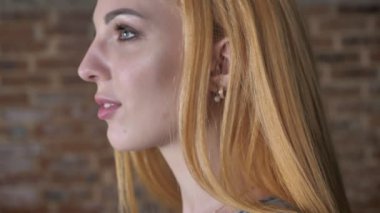 Genç mutlu sarışın kız gülümsüyor, tuğla arka plan baş amd kameraya, izlerken dönüyor