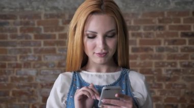 Genç çekici sarışın kız izlerken kamera, tuğla arka plan, iletişim kavramı smartphone, ileti yazmakta olduğunu