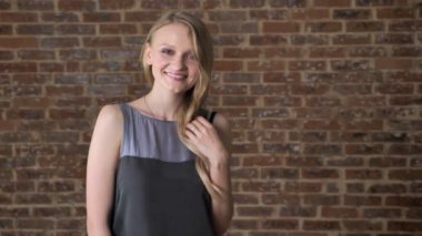 Genç Sevimli utangaç sarışın kız oynamaya saç, flört kavramı, tuğla arka plan