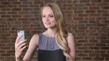Genç Sevimli sarışın kız smartphone, iletişim kavramı, tuğla arka plan video çağrısı var