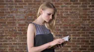 Genç çekici sarışın kız kameraya, tuğla arka plan izlerken kitap okuma