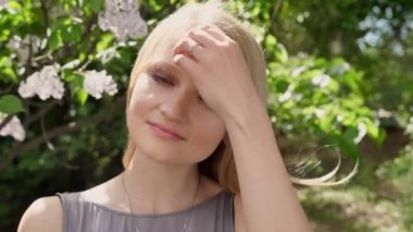Genç Sevimli sarışın kız kamera parkta gündüz yaz, gülümseyen, touchig saç izliyor