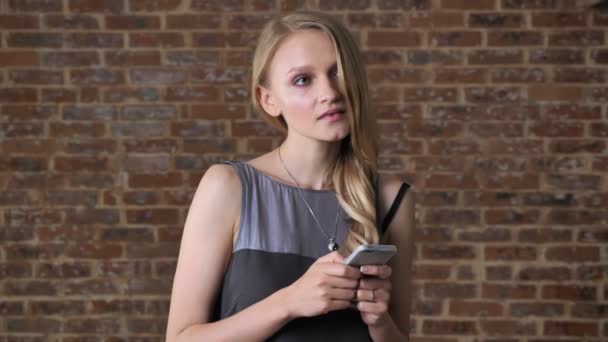 Jeune fille blonde mignonne tape message sur smartphone, concept de pensée, concept de communication, fond de brique — Video