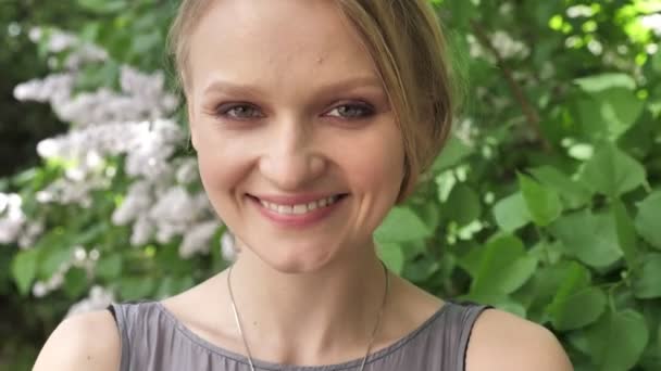 Jeune fille blonde mignonne regarde à la caméra dans le parc en journée en été, souriant — Video