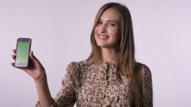 Genç güzel kadın gülümsüyor, saatler kamera, iletişim kavramı, beyaz arka plan, akıllı telefon, yeşil ekran gösterir