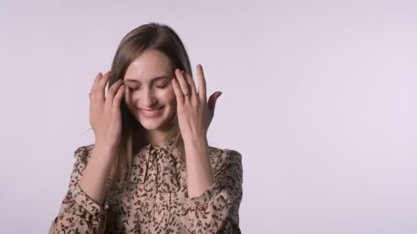 Joven mujer bastante inspirada está empujando el pelo, mirando a la cámara, sonriendo, fondo blanco — Vídeos de Stock