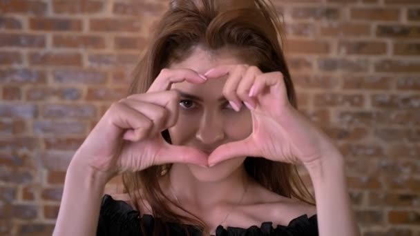 Sexy vrouw vertoont hart met vingers, een kus, een flirt concept, een communicatieconcept, een baksteen achtergrond — Stockvideo