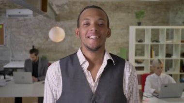 Genç Afrika işadamı duruyor ve gülüyor, ofis, kameraya izlerken meslektaşları ile dizüstü bilgisayarlar, iş kavramı çalışıyoruz