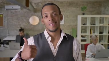 Genç Afrika işadamı duruyor ve işaret gibi gösteren kamera ofis, izlerken meslektaşları ile dizüstü bilgisayarlar, iş kavramı çalışıyoruz