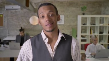 Genç Afrika işadamı duruyor ve ofis, gülümseyen, işaret gibi gösteren kamera izlerken meslektaşları ile dizüstü bilgisayarlar, iş kavramı çalışıyoruz.