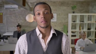 Yakışıklı Afrika işadamı duruyor ve ofis, gülümseyen, işaret gibi gösteren kamera izlerken meslektaşları ile dizüstü bilgisayarlar, iş kavramı çalışıyoruz