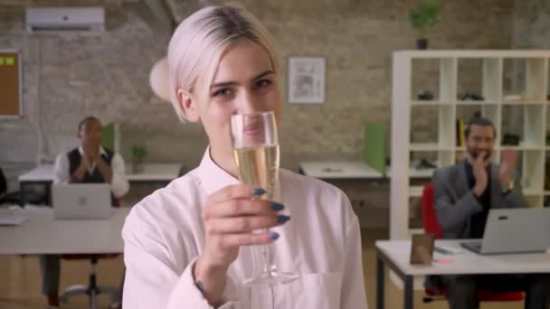 かなり若い実業家が立っているとオフィス 笑みを浮かべて シャンパンのグラスを保持している同僚が拍手 企業パーティー コンセプト — ストック動画