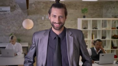 Sakallı mutlu işadamı ile geçti silah duruyor ve ofis, kameraya gülümseyen, izlerken meslektaşları ile dizüstü bilgisayarlar, iş kavramı çalışıyoruz