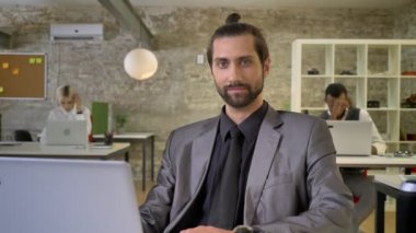 Kendine güvenen işkadını sakallı oturuyor laptop gülümseyerek kameraya izlerken ofiste iş arkadaşları ile iş kavramı, ağ teknolojileriyle iletişim kavramı.