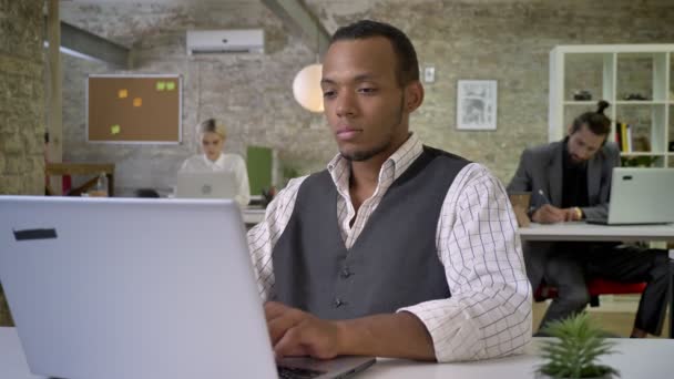 Jovem empresária africana está digitando no laptop no escritório, colegas estão trabalhando em rede com tecnologias, conceito de trabalho, conceito de comunicação — Vídeo de Stock