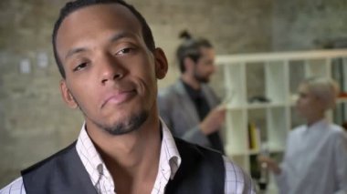 Genç Afrika işadamı duruyor ve kamera Office izlerken, meslektaşları konuşmak ve arka plan, iletişim kavramı, şirket parti kavramı şampanya içmek