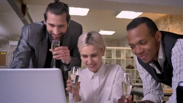 Três trabalhadores multy-étnicos estão assistindo na tela do laptop, beber champanhe, conceito do partido da empresa, conceito de comunicação — Vídeo de Stock