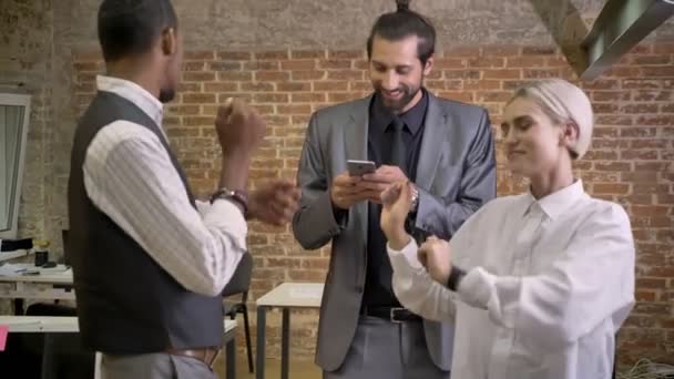 Tres trabajadores multiétnicos bailando en la oficina, viendo smartphone, concepto de fiesta de la empresa — Vídeo de stock