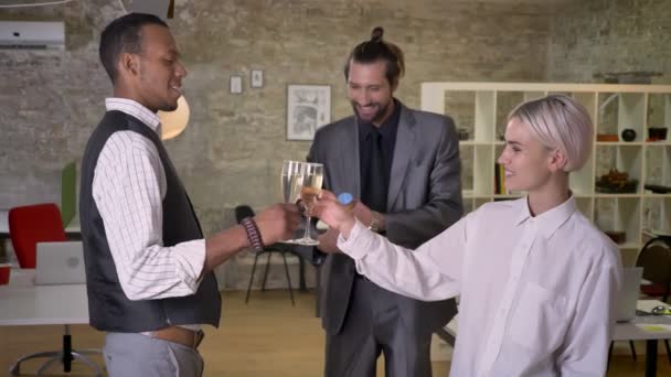 Три мультиэтнических работника звонят в стаканы, пьют шампанское в офисе, крэкеры, коммуникационная концепция, корпоративная вечеринка — стоковое видео