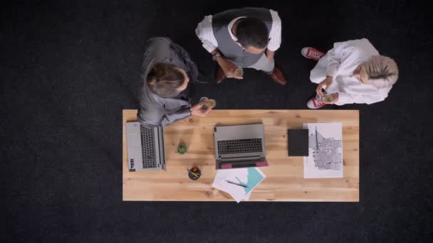 Три багатоетнічні працівники стоять в келихах шампанського біля столу з ноутбуками в офісі, концепцією вечірки компанії, концепцією комунікації, верхнім пострілом — стокове відео