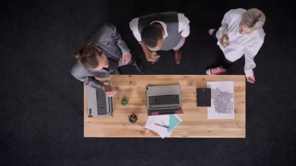 Tres trabajadores multiétnicos están bailando con copas de champán cerca de la mesa con computadoras portátiles en la oficina, concepto de fiesta de la empresa, concepto de comunicación, plano superior — Vídeos de Stock