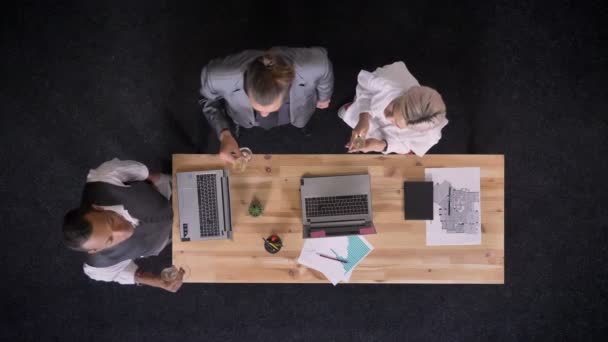 Три мультиэтнических работника разговаривают и хлопают бокалами шампанского возле стола с ноутбуками в офисе, концепция корпоративной вечеринки, коммуникационная концепция, топ-кадр — стоковое видео